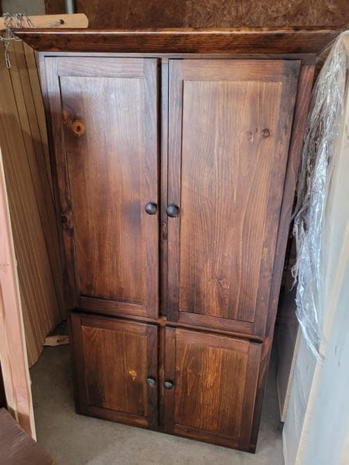 Walnut stained wooden pantry cabinet with two doors and knobs.