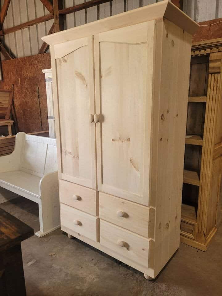 Unfinished wooden pantry cabinet with storage drawers and doors in workshop.